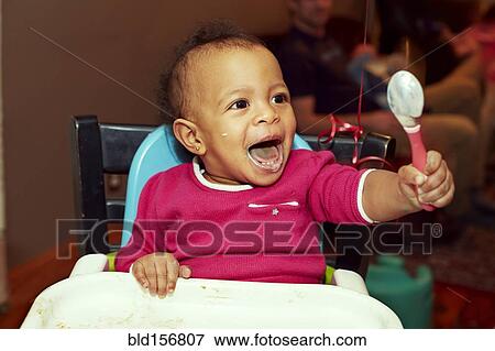 Stock Photo - Mixed race girl playing with spoon in high chair. Fotosearch