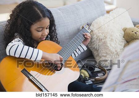 Stock Photography - Mixed race girl practicing guitar on sofa. Fotosearch