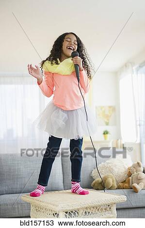 Mixed race girl singing on living room table View Large Photo Image Stock Image - Mixed race girl singing on living room table. Fotosearch