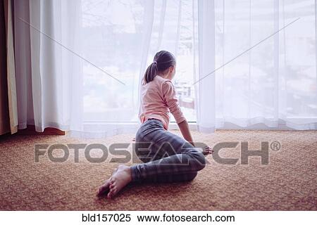 Stock Photography - Mixed race girl sitting on floor looking out window. Fotosearch