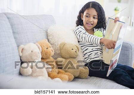 Stock Image - Mixed race girl teaching teddy bears on sofa. Fotosearch