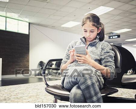Stock Image - Mixed race girl using cell phone in airport. Fotosearch