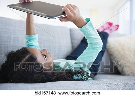 Stock Photo - Mixed race girl using digital tablet on sofa. Fotosearch