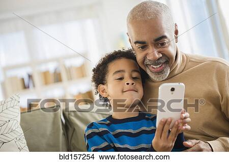 Mixed race grandfather and grandson using cell phone View Large Photo Image Picture - Mixed race grandfather and grandson using cell phone. Fotosearch