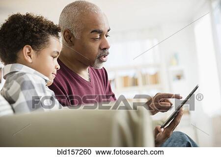 Stock Image - Mixed race grandfather and grandson using digital tablet. Fotosearch