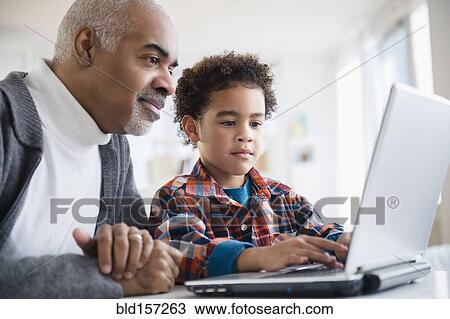 Stock Image - Mixed race grandfather and grandson using laptop. Fotosearch