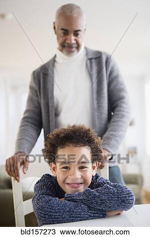 Stock Image - Mixed race grandfather and grandson sitting at table. Fotosearch