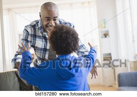 Stock Image - Mixed race grandfather and grandson greeting in living room. Fotosearch