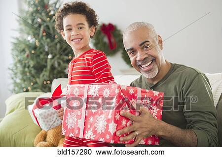 Stock Image - Mixed race grandfather and grandson opening Christmas gifts. Fotosearch