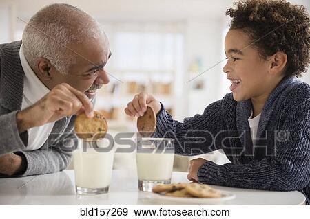 Stock Photo - Mixed race grandfather and grandson eating cookies and milk. Fotosearch