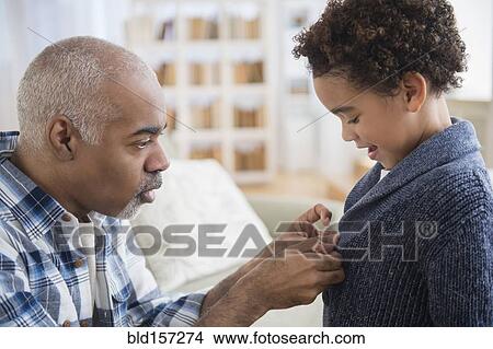 Picture - Mixed race grandfather buttoning sweater for grandson. Fotosearch