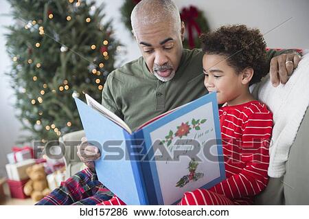 Stock Photograph - Mixed race grandfather reading to grandson at Christmas. Fotosearch