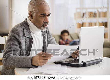 Stock Photo - Mixed race man paying bills on laptop. Fotosearch