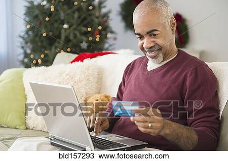 Stock Image - Mixed race man shopping online with laptop at Christmas. Fotosearch
