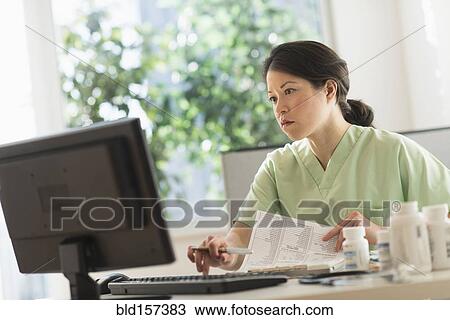 Stock Image - Mixed race nurse working on computer in hospital. Fotosearch
