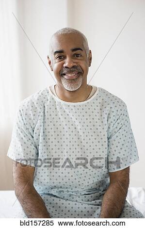 Stock Photography - Mixed race older man sitting on hospital bed. Fotosearch