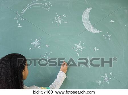 Stock Image - Mixed race student drawing stars on chalkboard in classroom. Fotosearch