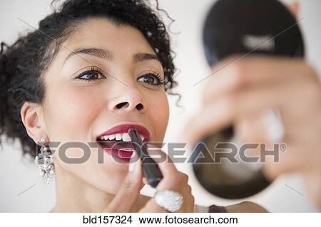 Picture - Mixed race woman applying lipstick in compact mirror. Fotosearch