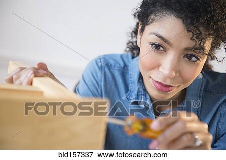 Stock Photo - Mixed race woman assembling furniture. Fotosearch