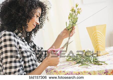 Stock Photograph - Mixed race woman cutting flower stems at table. Fotosearch
