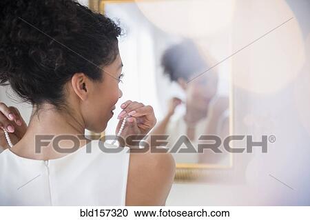 Mixed race woman fastening pearl necklace in mirror View Large Photo Image Stock Image - Mixed race woman fastening pearl necklace in mirror. Fotosearch