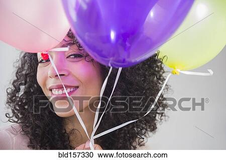 Stock Image - Mixed race woman holding bunch of balloons. Fotosearch