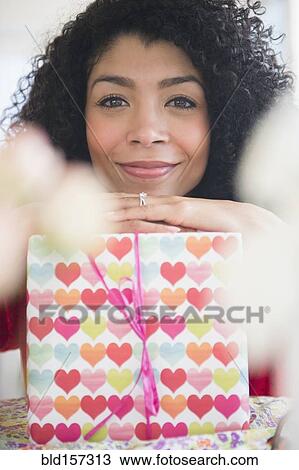 Stock Image - Mixed race woman holding wrapped gift. Fotosearch