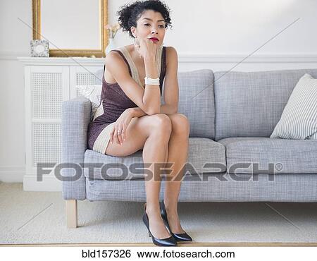 Stock Photograph - Mixed race woman in cocktail dress sitting on sofa. Fotosearch