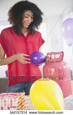 Picture - Mixed race woman inflating helium balloons for party. Fotosearch