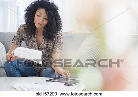 Stock Photo - Mixed race woman paying bills on digital tablet. Fotosearch
