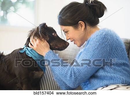 Picture - Mixed race woman petting dog on sofa. Fotosearch