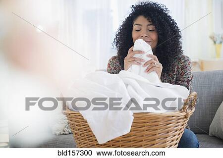 Stock Image - Mixed race woman smelling clean towels in laundry. Fotosearch