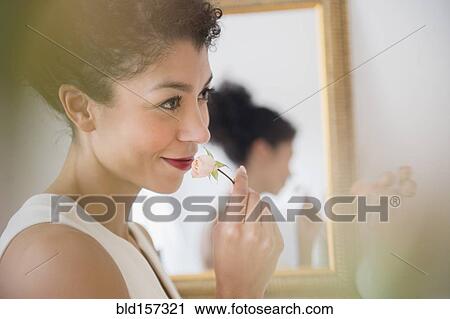 Stock Image - Mixed race woman smelling flower near mirror. Fotosearch