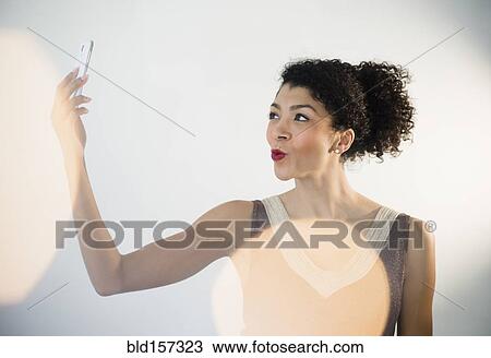 Stock Image - Mixed race woman taking cell phone selfie in evening gown. Fotosearch