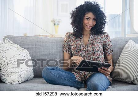 Stock Photo - Mixed race woman using digital tablet on sofa. Fotosearch