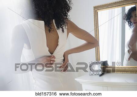 Stock Photograph - Mixed race woman zipping dress in mirror. Fotosearch