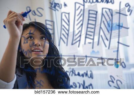 Stock Photograph - Pacific Islander businesswoman drawing chart on glass in office. Fotosearch