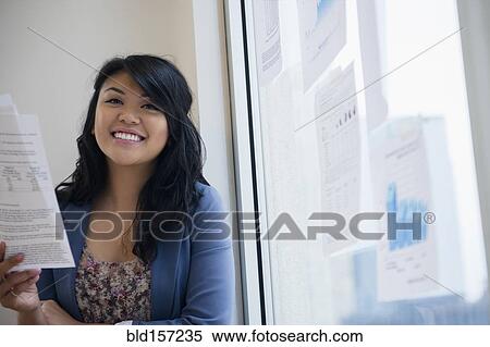 Stock Photography - Pacific Islander businesswoman reading paperwork near window. Fotosearch