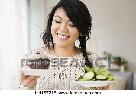 Stock Photo - Pacific Islander woman choosing between cupcake and salad. Fotosearch