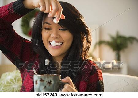 Stock Image - Pacific Islander woman dropping marshmallows into hot chocolate. Fotosearch