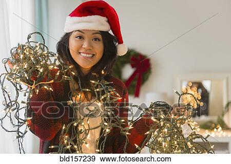 Stock Photo - Pacific Islander woman in Santa hat holding string lights. Fotosearch