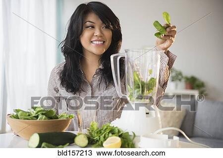 Stock Image - Pacific Islander woman making green smoothie in blender. Fotosearch