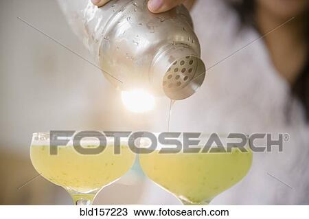 Stock Image - Pacific Islander woman pouring cocktails from shaker. Fotosearch
