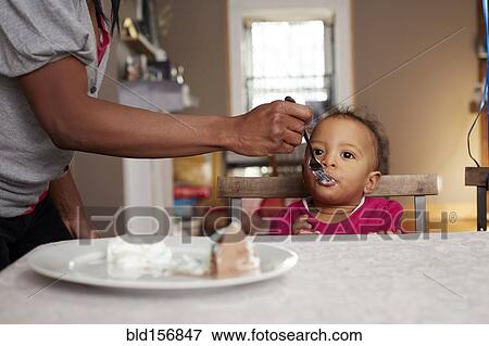 Stock Photo - Parent feeing daughter cake at table. Fotosearch