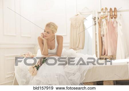 Stock Photo - Pensive bride sitting with bouquet on bed. Fotosearch