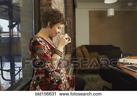 Stock Image - Pregnant businesswoman drinking coffee in office. Fotosearch