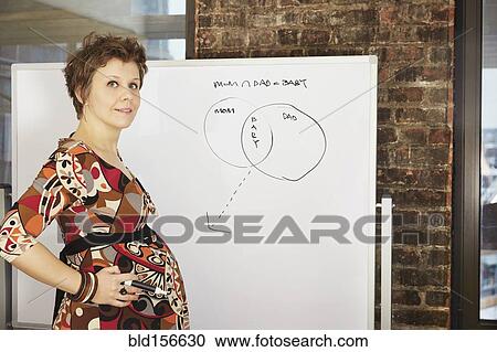Stock Image - Pregnant businesswoman standing near whiteboard in office. Fotosearch