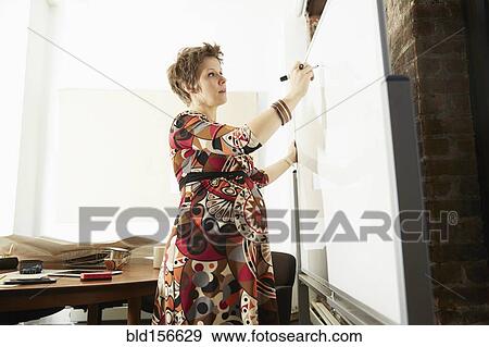 Stock Photo - Pregnant businesswoman writing on whiteboard in office. Fotosearch