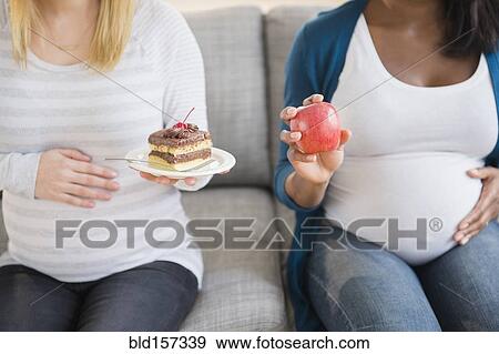 Pregnant women comparing apple and cake on sofa View Large Photo Image Stock Photo - Pregnant women comparing apple and cake on sofa. Fotosearch