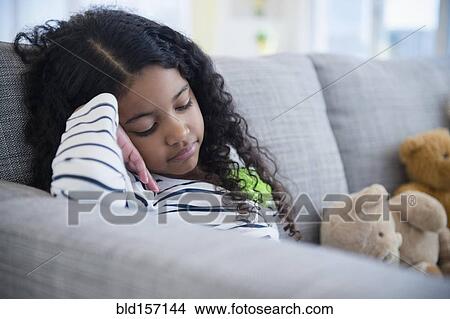 Picture - Sad mixed race girl sitting on sofa. Fotosearch